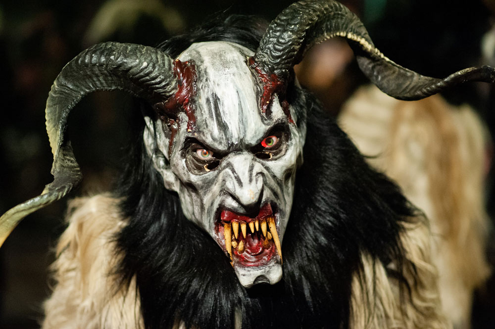 If you're looking to experience unique winter traditions in Europe beyond the usual Christmas markets, Austria is the perfect destination. The following chapters will give you an idea of what is the Krampus Parade in Austria, where and when it happens. Origins Krampus is a mythological figure with horns that usually accompanies St. Nicholas on the night of the 5th to 6th of December. They both are central figures in Central and Eastern European winter traditions. They visit small children and evaluate their behavior. St. Nicholas rewards the good ones, while Krampus punishes those naughty ones. Krampus usually uses birch rods and coal. The Word Krampus originated in Bavarian - krampn, meaning the dead, or in German - kramp-en, meaning claw. People portray Krampus in a way that mirrors our usual imagery of the devil or demons. Half-man, half-goat. An anthropomorphic persona with horns, fur, a hooked nose, a beard, dark hair, and a long tongue. Some people suggest that his look has some antisemitic vibes, particularly the portrayal of the hooked nose. Although the Krampus should represent the otherness, there are often subtle signs that resemble the antisemitic depictions of Jews. At a certain point in history, Catholic traditions merged with the pagan customs already in the Alpine regions. People would mask themselves as devils, don animal furs, and participate in a procession called **Perchtenlaufen**, an ancient pagan ritual. This blending of traditions is often seen as the precursor to today's Krampus Parades. Villagers believed Krampus and his perchten roamed the Tyrolean Alps causing chaos, while parents used his legend to scare children into good behavior. Today, Krampus is celebrated as a rebellious anti-hero in festive events, embraced by Tyroleans as a symbol of defiance against the commercialized Santa Claus. Krampus Parades A big part of the parade is the Krampuslauf or the Krampus Run. All the participants dressed in masks run down the streets and chase the spectators. They may growl, shake chains, or move sticks and whips. When looking at some older footage, they all seem to act and behave quite dangerously and create an aura of fear around them. Krampuses also act out certain scenes and try to interact with the crowd. They can punish the naughty children or perform playful acts of mischief. There have been reports of some spectators reacting angrily to the Krampuses' playful whipping, leading to altercations. In some instances, these confrontations escalated, with several people reportedly ending up in the hospital with broken bones. The parades also try to showcase the Krampus costumes. The costumes and masks are usually handcrafted, including horns, bells, and fur. Fire shows and drumming are another popular aspects of the parades. The drumming tends to establish a tribal and intense atmosphere. After the Krampus Run, you can continue and enjoy yourself at the after-party at the local market, stall, or pub. Traditional Austrian fare, including sausages, mulled wine, and pastries, is typically served. Where and when The above lines have outlined what is the Krampus Parade in Austria, but now is the time to find out when and where they happen. It is usually early December (5th, 6th),  in some cases late November when cities like Salzburg, Innsbruck, Graz, Klagenfurt, Villach, Bad Gastein, Bischofshofen, St. Johann im Pongau, Telfs (Tyrol) host this wild festivities. Many of them concentrate in the city centers and near Christmas markets. The parades always happen during the night. The most famous one is in Salzburg, the family-friendly one in Graz, and the oldest in St. Johann im Pongau.